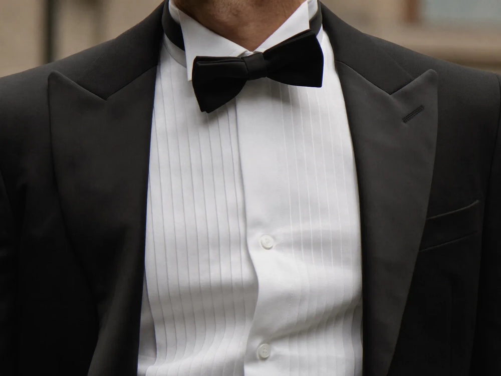 A man wearing a white tuxedo shirt with a black bow tie under an open black tuxedo jacket