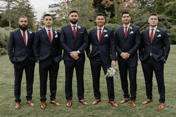 A groom and groomsmen in coordinated navy suits at an outdoor wedding