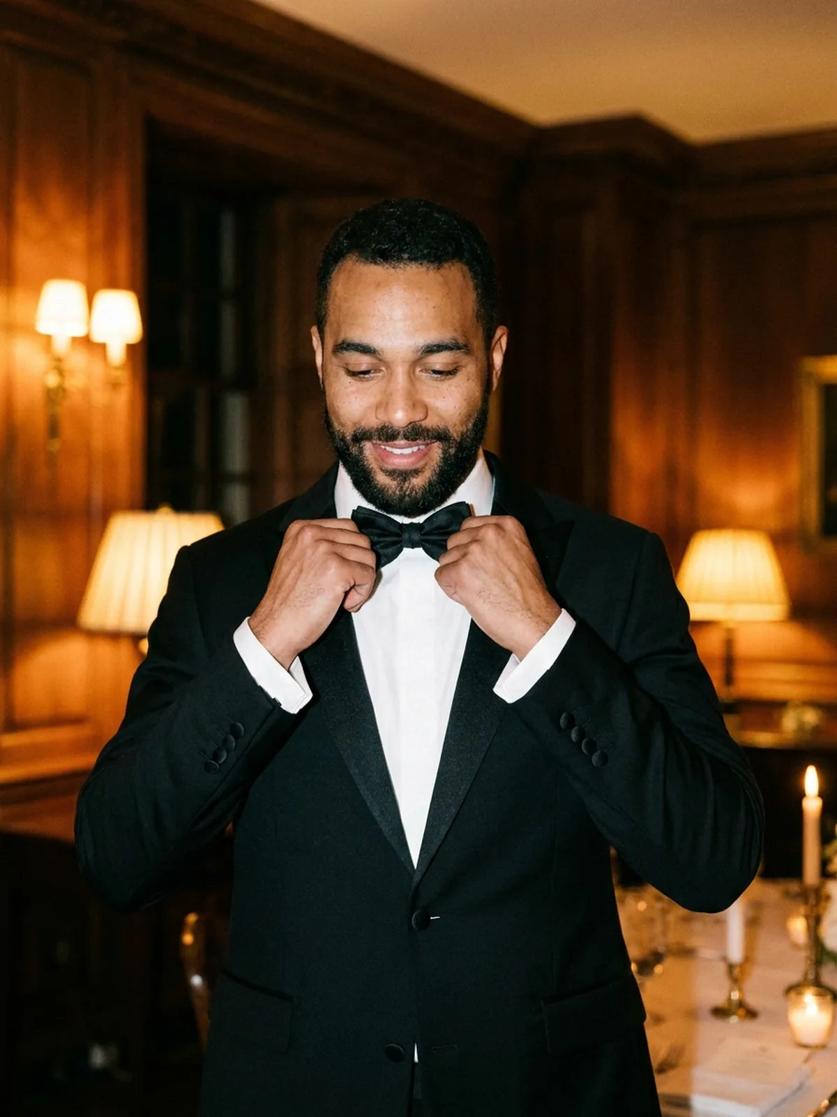 A man adjusting his black bow tie while wearing a tuxedo.