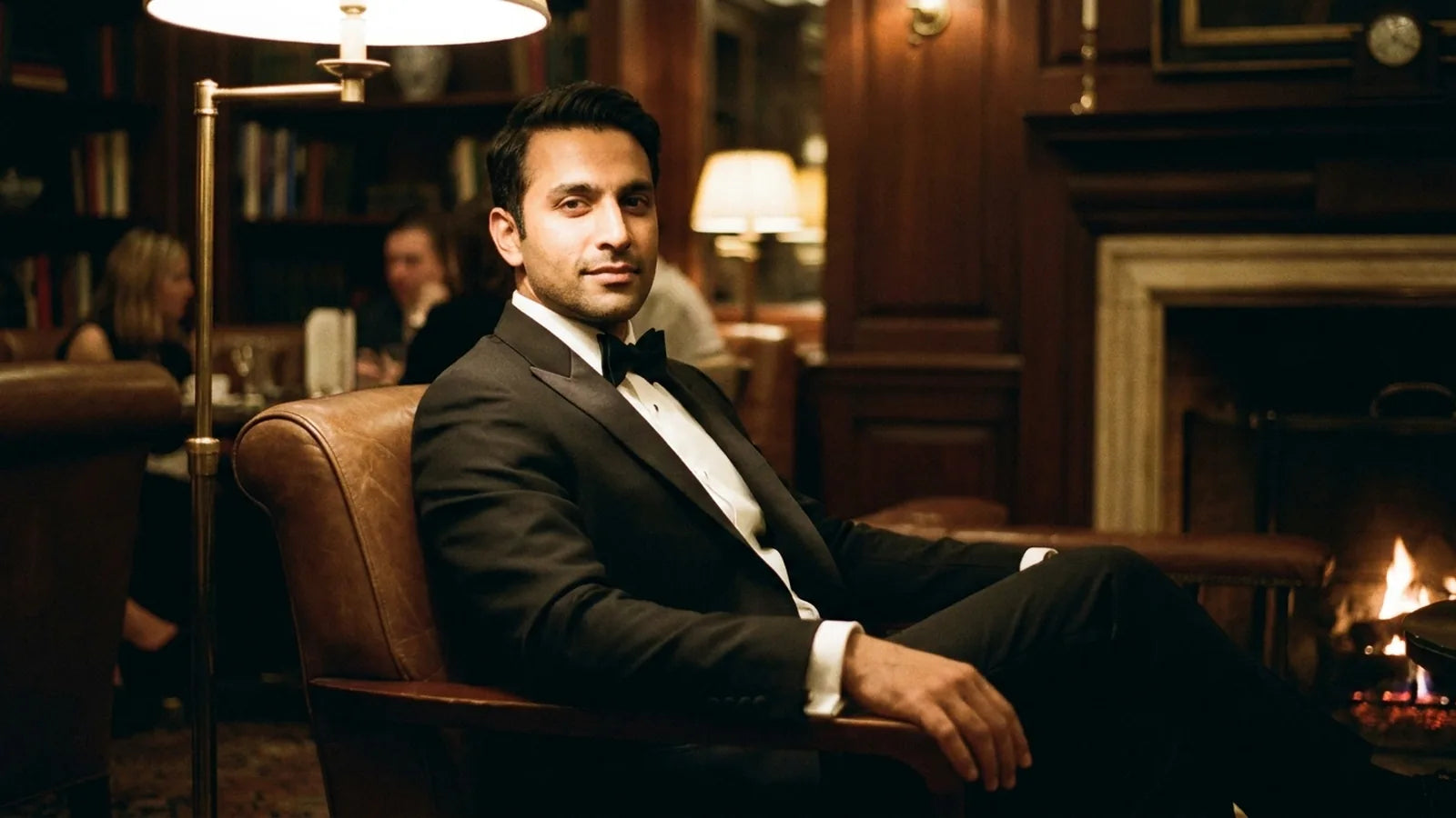 A man in a classic black tuxedo seated in a warm evening lounge.