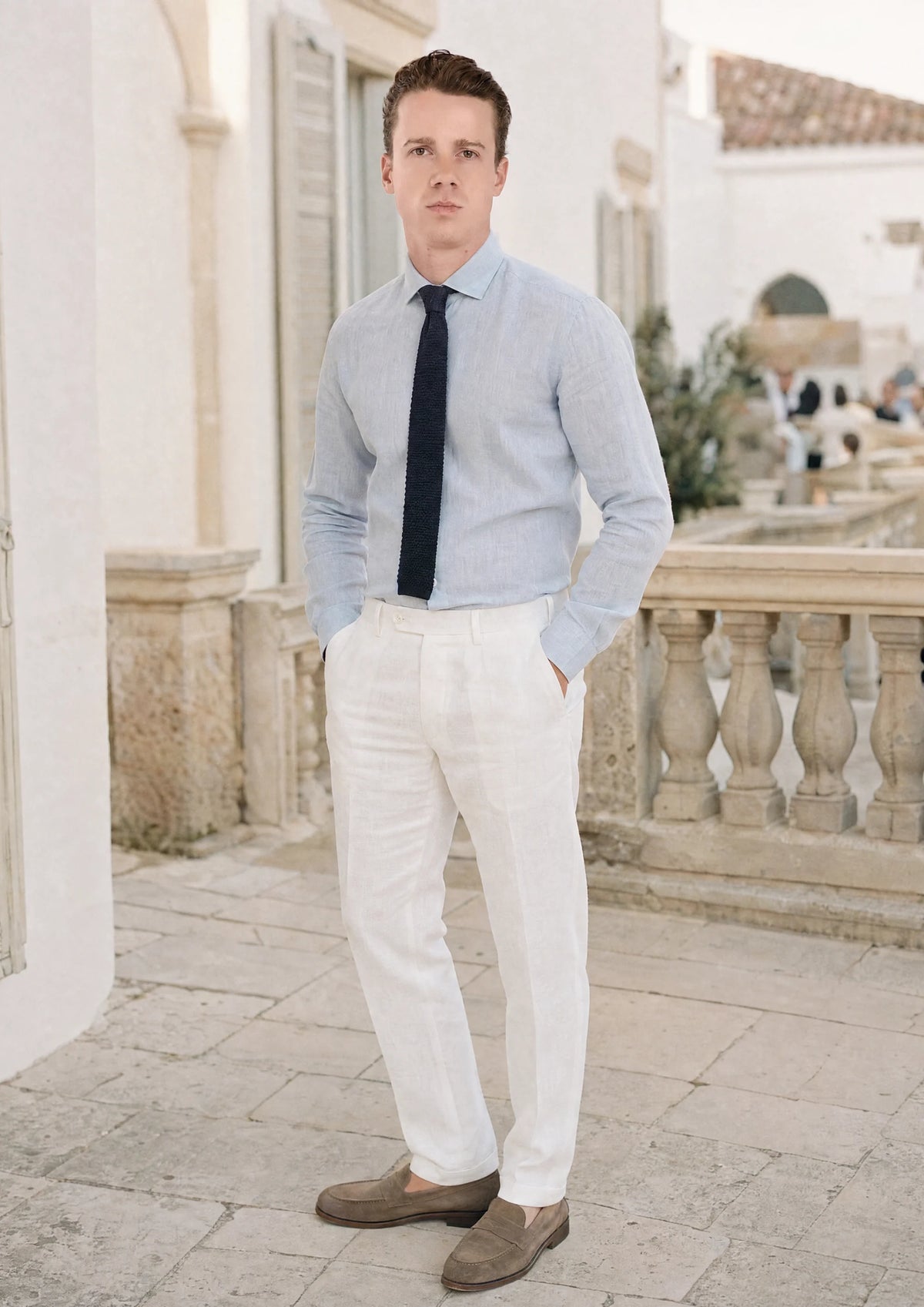 Man in white linen trousers and pale blue shirt on a villa terrace at a summer wedding942