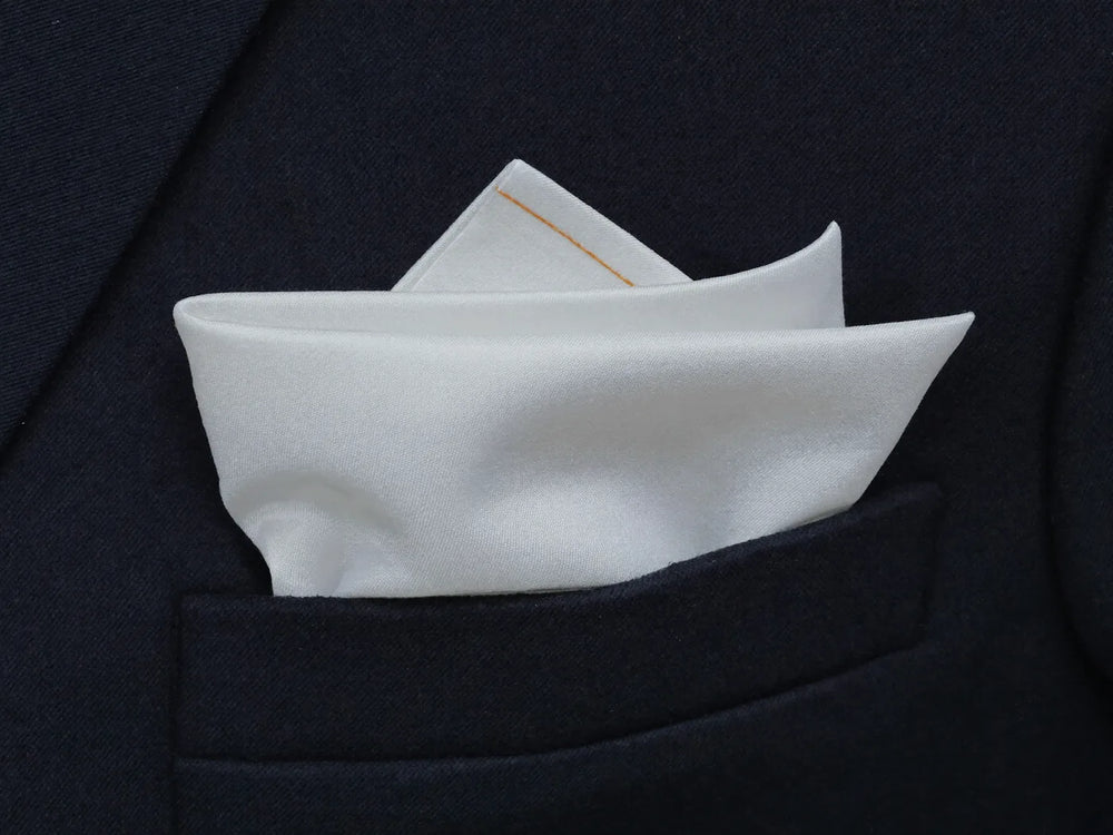 A white pocket square folded in the breast pocket of a navy suit jacket