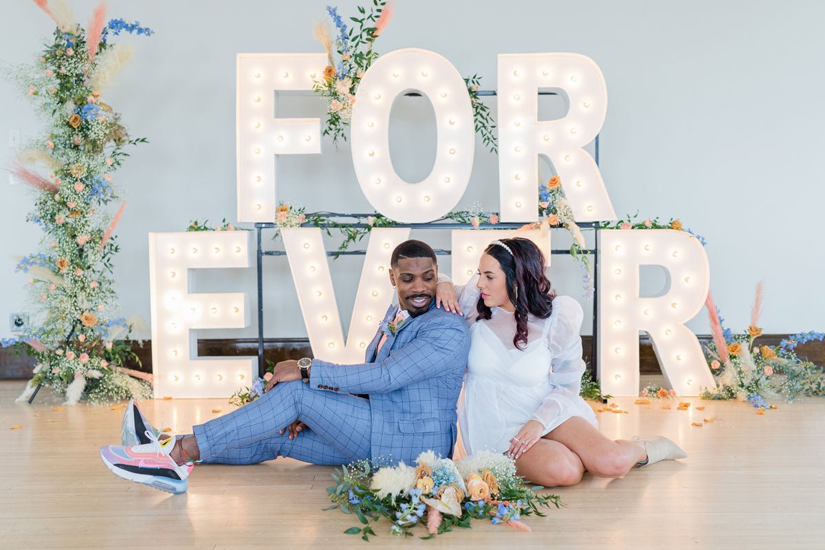 wedding couple sitting on ground in front of a sign that says FOREVER