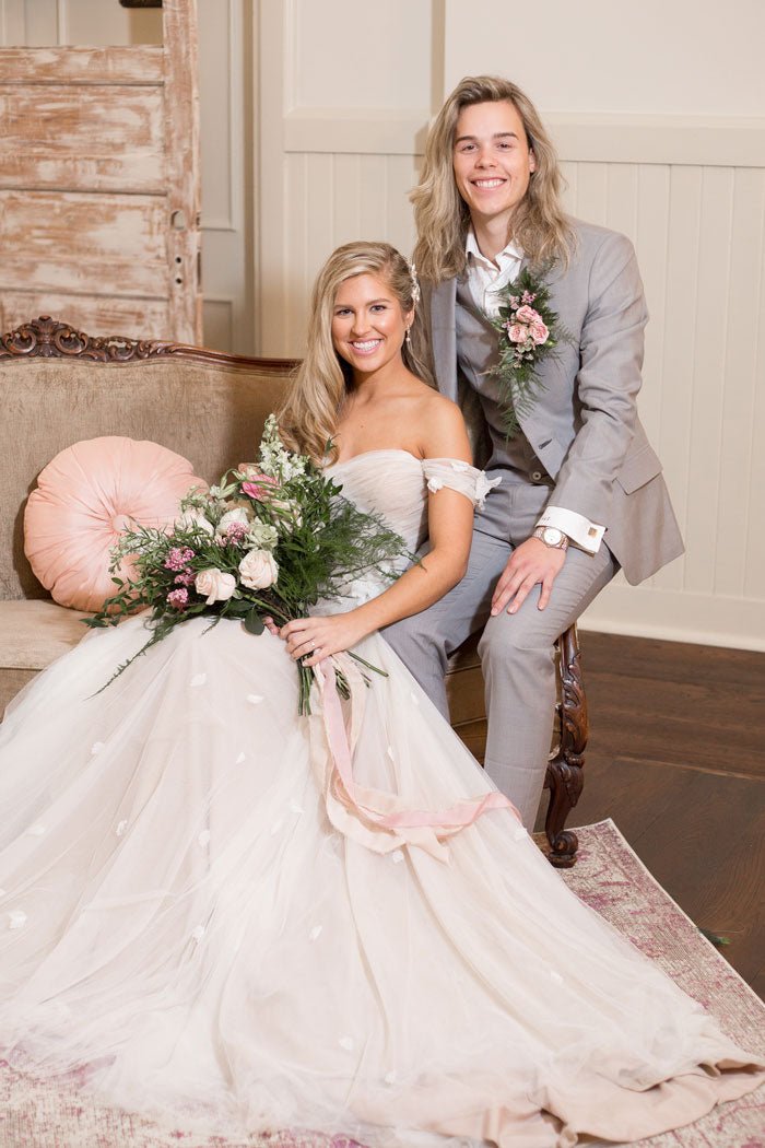 bride and groom sitting together on couch. groom in a grey three piece suit