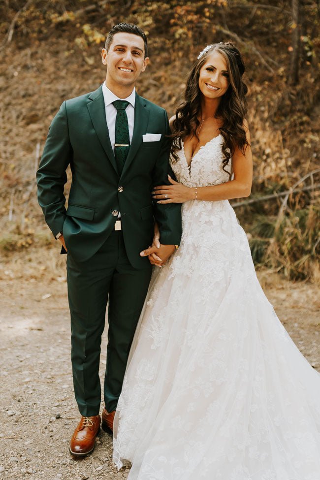 bride and groom holding hands and posing. green suit and white dress.