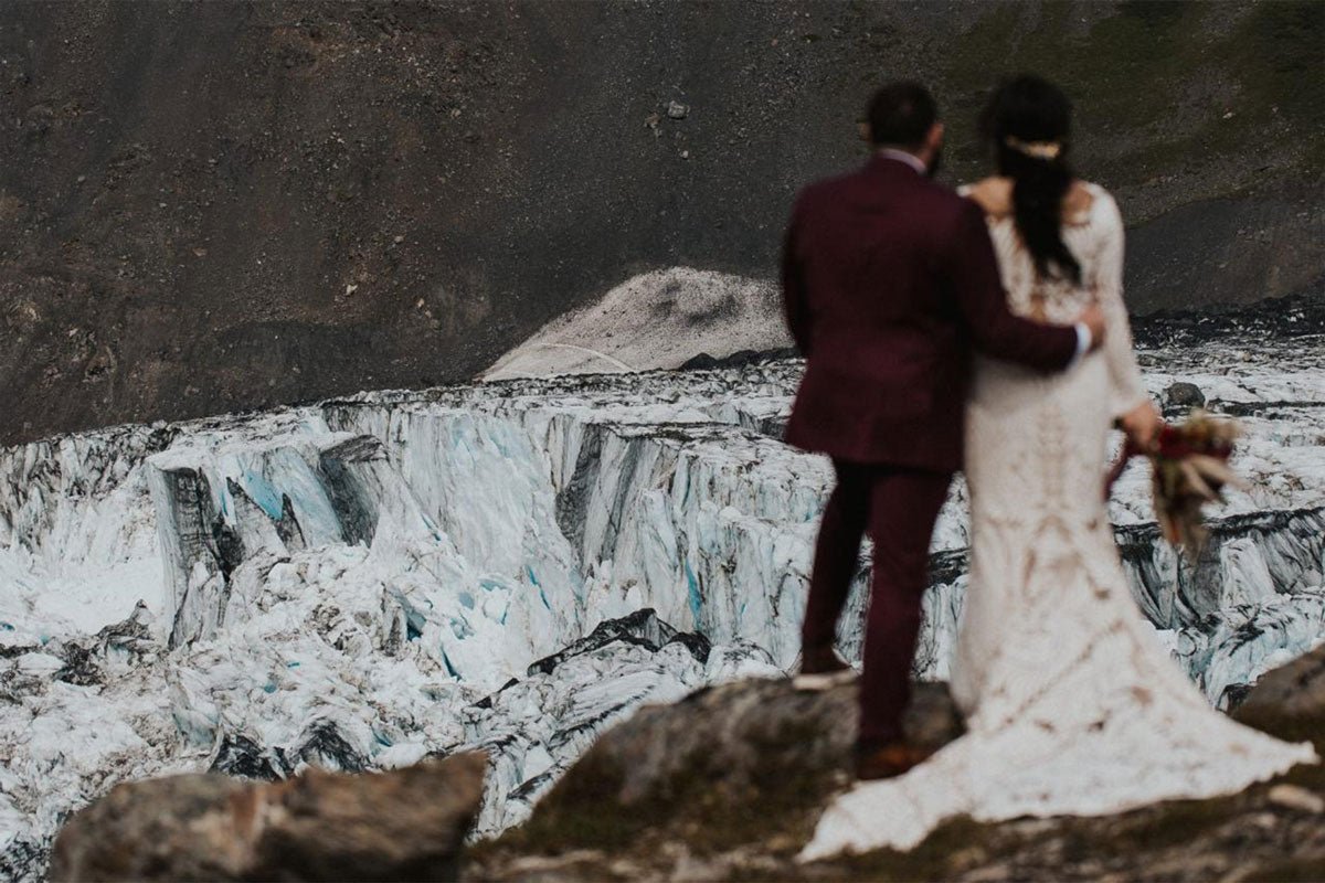 bride and groom standing on a cliff edge overlooking a massive glacier