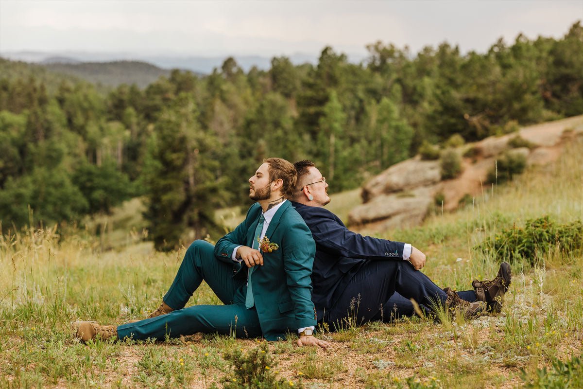 two grooms sitting back to back on the ground in the countryside