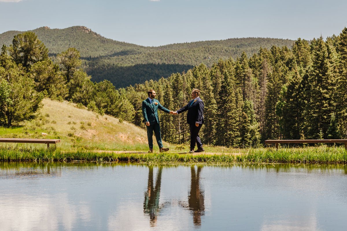 two grooms holding hands next to a pond