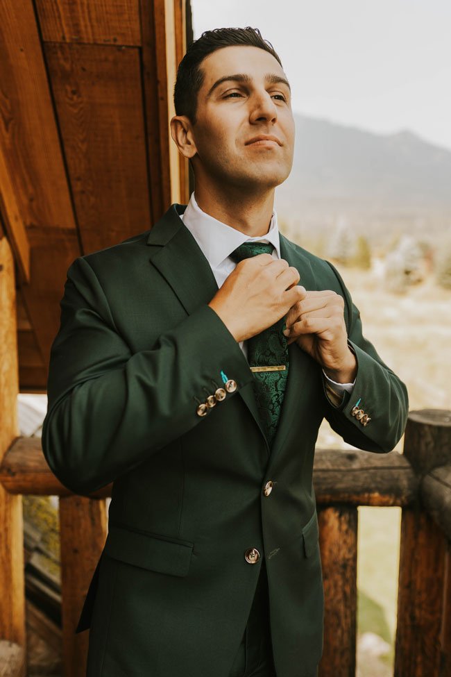 groom adjusting his green tie in his green suit