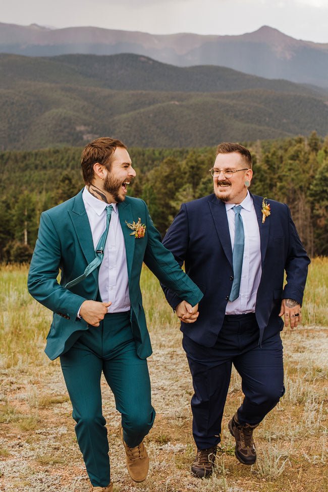 two grooms holding hands and running up the hillside in their wedding suits