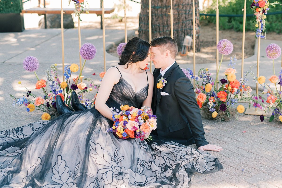 bride and groom sitting on the ground embracing around flowers