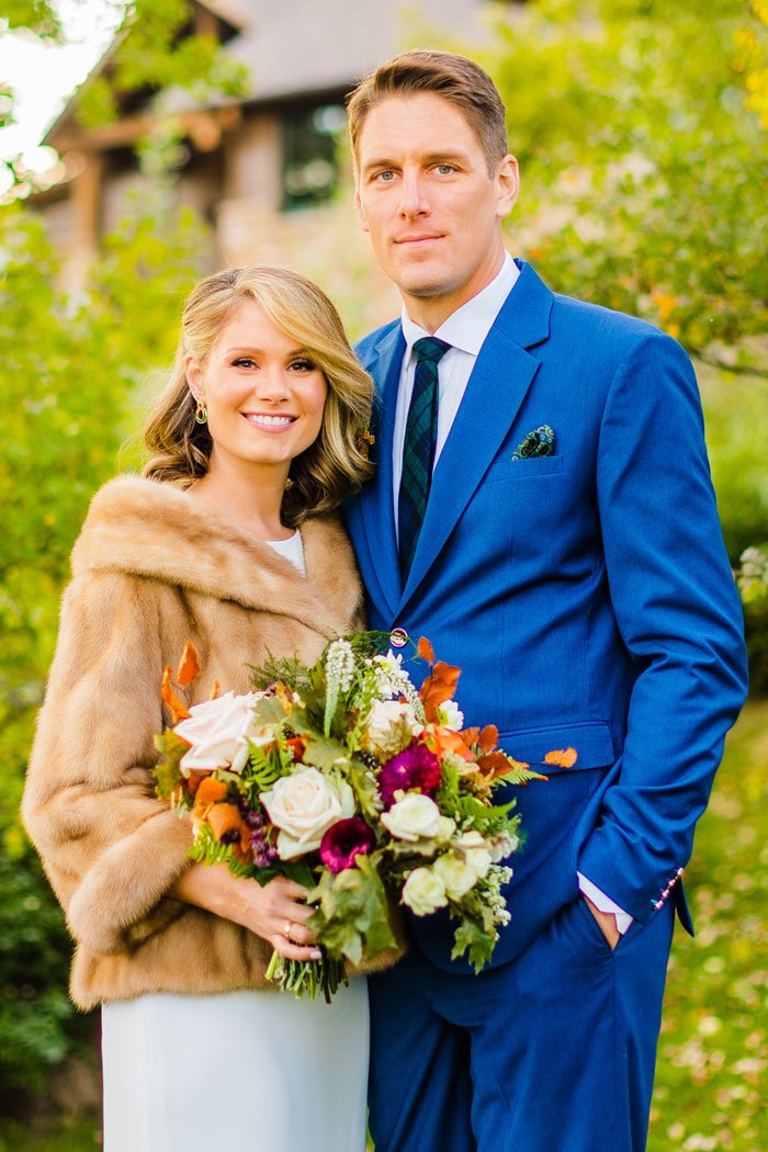 bride and groom posing after getting married. groom in blue suit, bride in white dress and brown fur coat