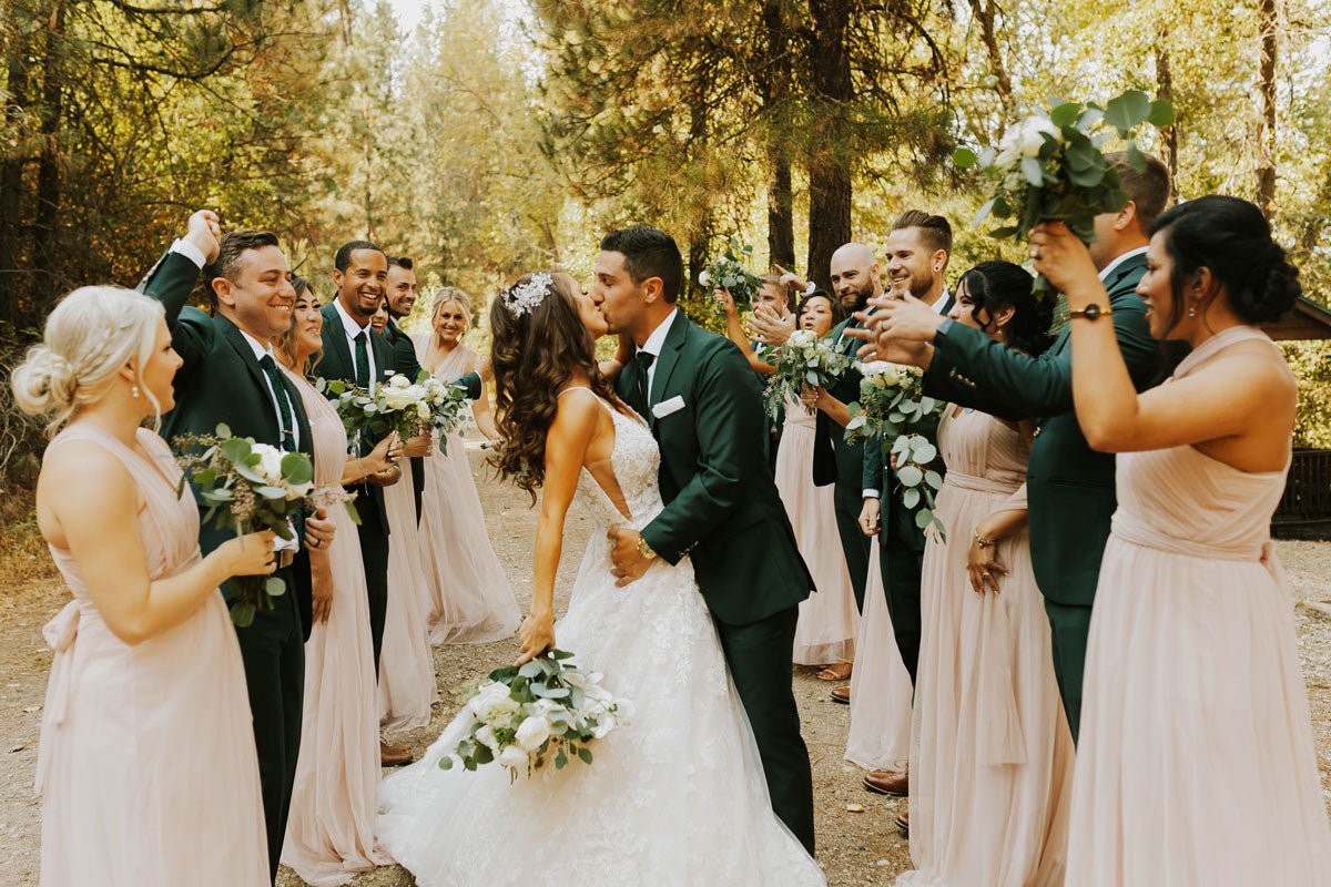 bride and groom kissing as the wedding party cheers them on in green suits