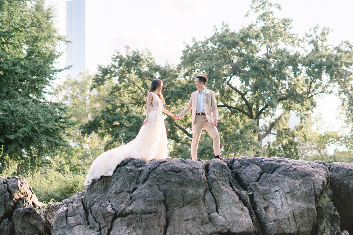 wedding couple holding hands on top of big rock in central park