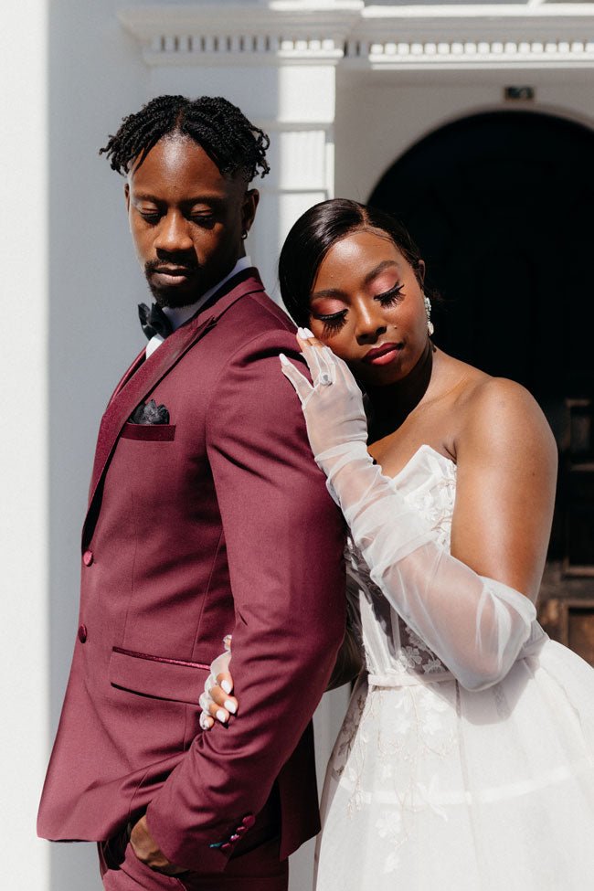 bride and groom embracing in front of a doorway. burgundy tuxedo