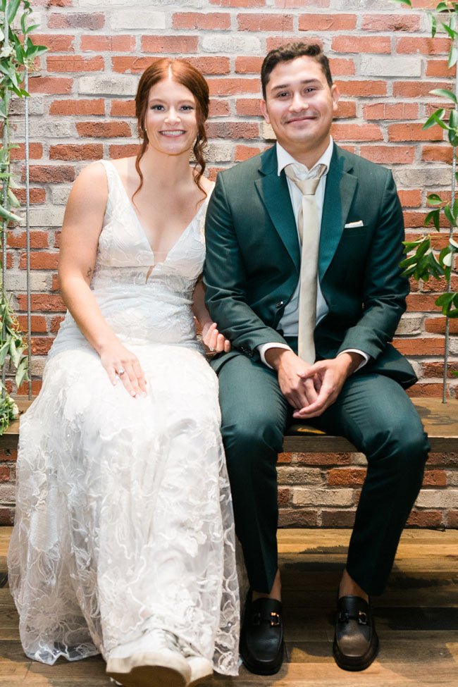 bride and groom sitting on bench. green suit.