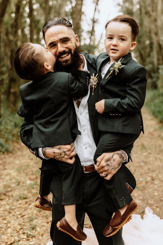 groom holding his two toddlers, all wearing matching green suits