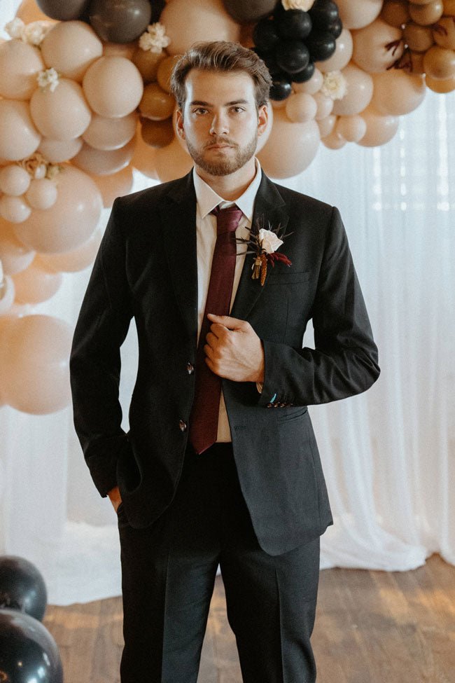 groom in black suit in front of balloons