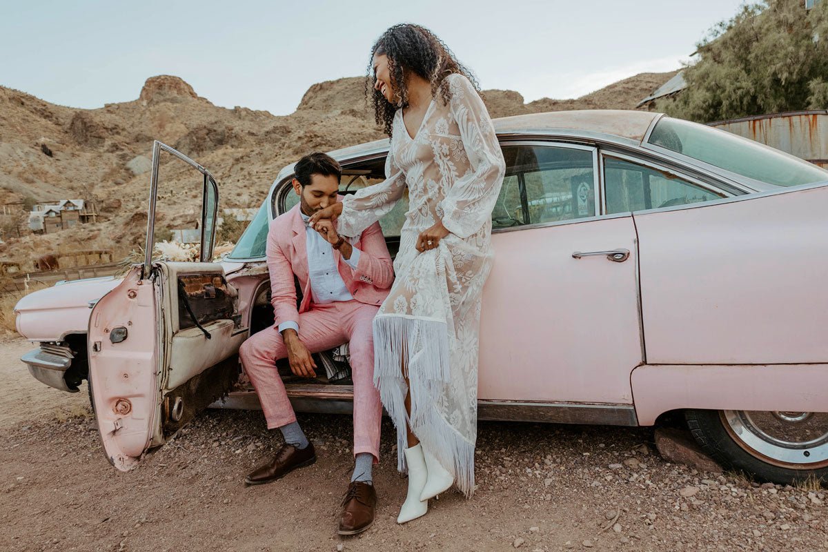 groom popping open a bottle of champagne while his bride looks on