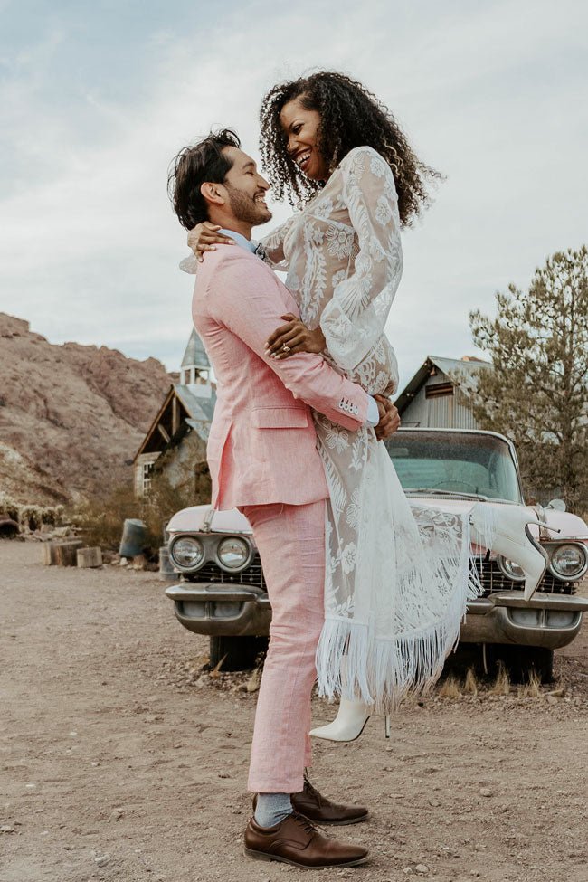 groom picking up bride in front of a car in ghost town