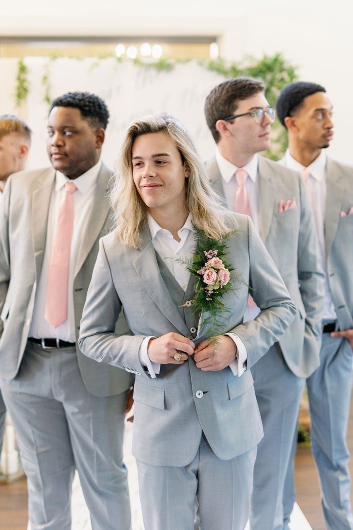 groom smiling in three piece grey suit with groomsmen behind him